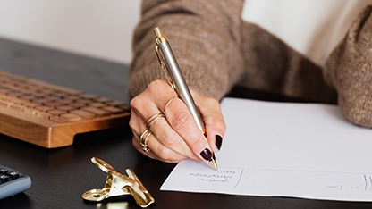 Ett fotografi på en hand som skriver på ett papper med en penna.