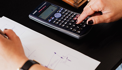 En bild på en hand som trycker på en miniräknare och som skriver på ett papper.