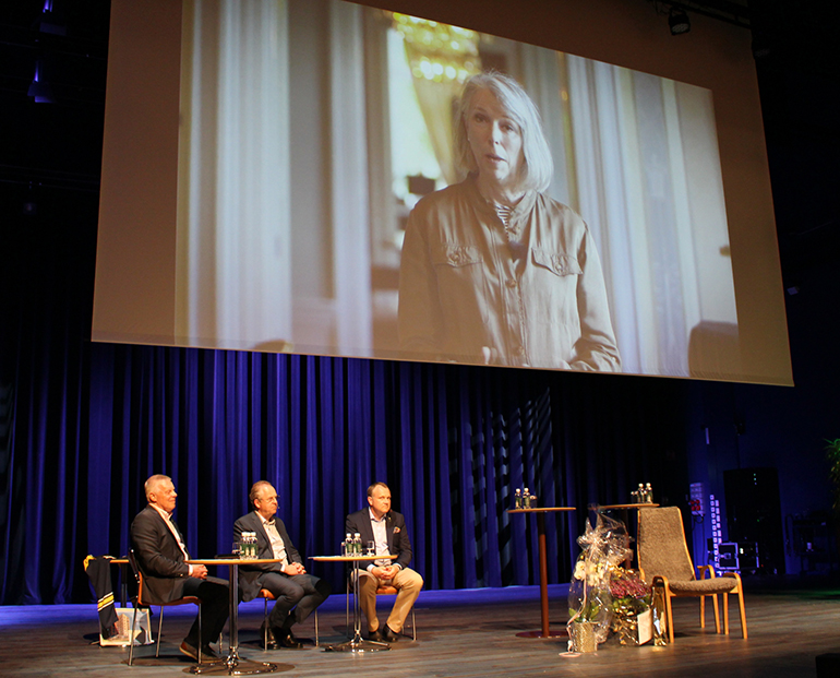 Bild som visar landshövding Helena Jonsson på storbildsskärm. På scenen under skärmen sitter Hans-Göran Johansson, Ulf Svensson och Mikael Karlsson.