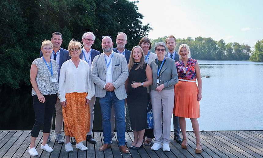 Flera pesoner står samlade i en grupp på en träbrygga. I bakgrunden syns sjön Bolmen. Det är vackert sommarväder.