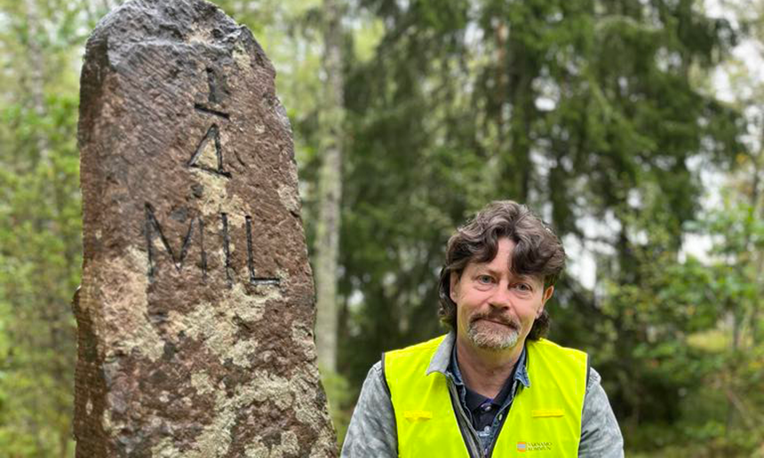 Närbild på Peter Andersson som står intill milstenen. På milstenen står det 1/4, vilket betyder en fjärdedels mil.