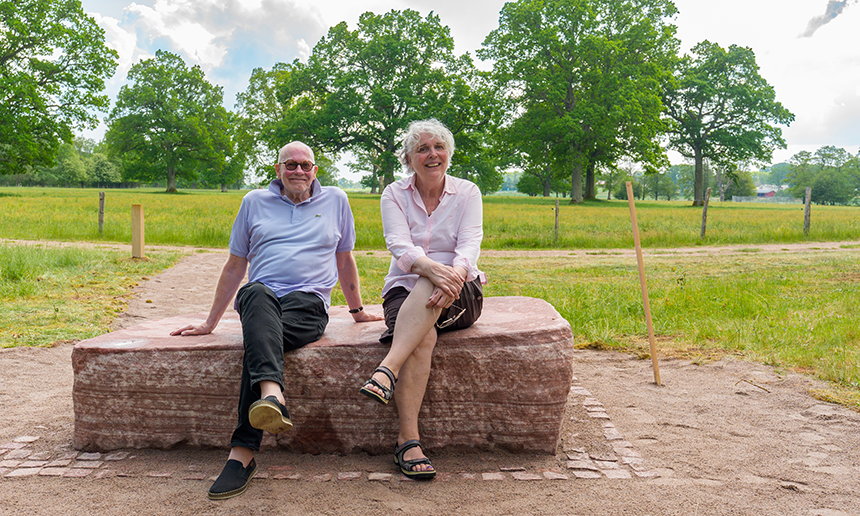 Två personer, donatorn och konstnären, sitter på konstverket, som är ett stort stenblock.