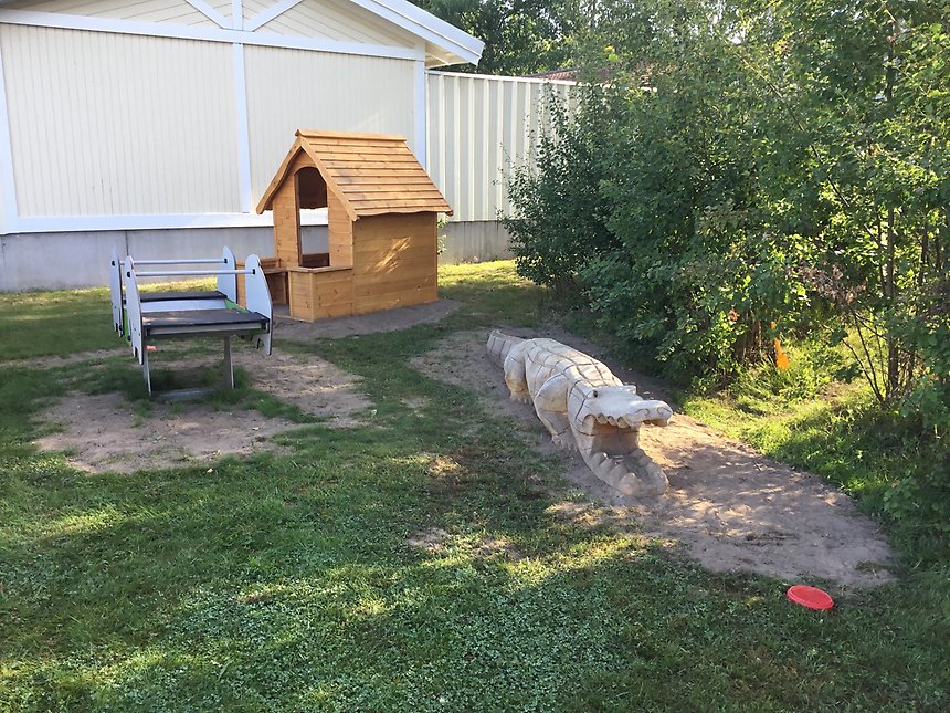 En bild från förskolans gård. Det finns en lekstuga och en krokodil i trä