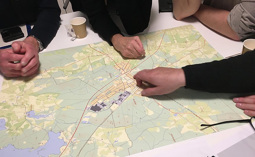 Ett bord med en karta där händer syns peka på olika platser.